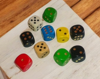 Könnte beinhalten: Zehn bunte Würfel mit schwarzen und goldenen Punkten. Die Würfel sind in einem Dreiecksmuster auf einer weißen Holzoberfläche angeordnet.