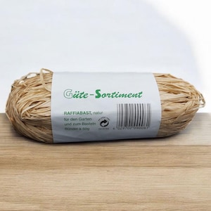 May include: A roll of natural raffia bast, a type of fibre used for gardening and crafting. The label reads "Güte-Sortiment Raffia bast, natur für den Garten und zum Basteln Bündel à 50g 4 029702 090061".