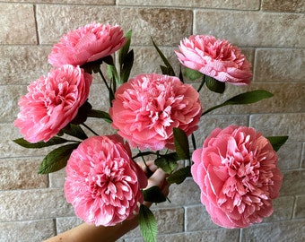 May include: A bouquet of six pink paper peonies with green stems and leaves.