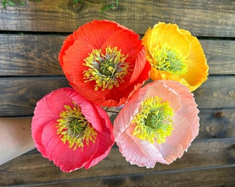 Könnte beinhalten: Vier Papierblumen in Rot-, Rosa- und Gelbtönen. Die Blumen haben eine geschichtete, gekräuselte Textur und ähneln Mohnblumen.