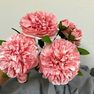 Op de afbeelding: Een boeket van vijf roze papieren pioenen met groene bladeren. De pioenen zijn gemaakt van tissuepapier en hebben een delicate, gekrulde textuur.