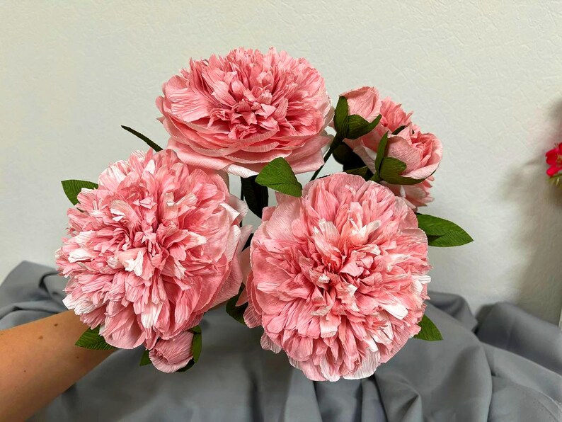 Op de afbeelding: Een boeket van vijf roze papieren pioenen met groene bladeren. De pioenen zijn gemaakt van tissuepapier en hebben een delicate, gekrulde textuur.