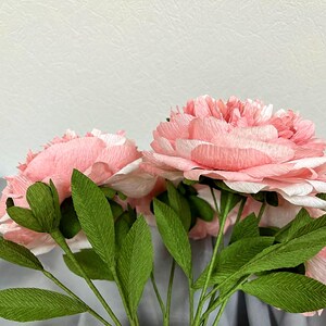 Op de afbeelding: Een boeket roze papieren pioenen met groene papieren bladeren.
