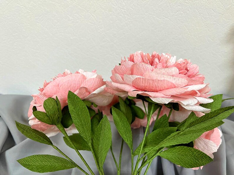 Op de afbeelding: Een boeket roze papieren pioenen met groene papieren bladeren.
