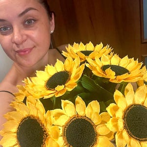 Peut inclure: Un bouquet de grands tournesols en papier avec des p&eacute;tales jaune vif et des centres brun fonc&eacute;. Les fleurs ont des feuilles de papier vertes. Le bouquet est tenu par une personne.