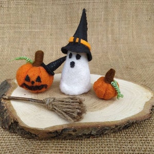 May include: A felt ghost wearing a black witch hat with an orange band, holding a small broom. Two orange felt pumpkins are on a wooden slice.