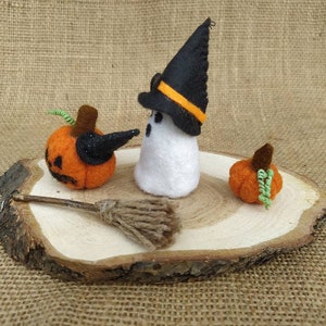 May include: Felt Halloween decorations on a wooden slice. A white ghost wearing a black witch hat with an orange stripe, a small orange pumpkin, and a larger orange pumpkin with a black witch hat.