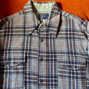 Peut inclure: Une chemise à carreaux boutonnée dans les tons de bleu, gris et marron. La chemise a deux poches de poitrine et un col avec une doublure matelassée. L'étiquette Pendleton est visible.