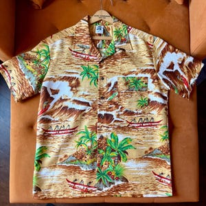 Op de afbeelding: Tan Hawaiiaans overhemd met een tropische print van palmbomen, kano's en oceaangolven. Het overhemd heeft korte mouwen, een knoopsluiting en een borstzak. Het overhemd hangt aan een houten kleerhanger.