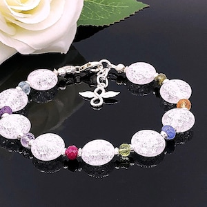May include: A bracelet with large, oval, crackled glass beads and smaller, colourful gemstone beads. It has a silver clasp and a decorative charm. A white rose is in the background. The bracelet is a piece of jewellery.