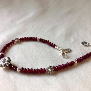 May include: A silver bracelet with a red gemstone bead chain and silver flower charms.
