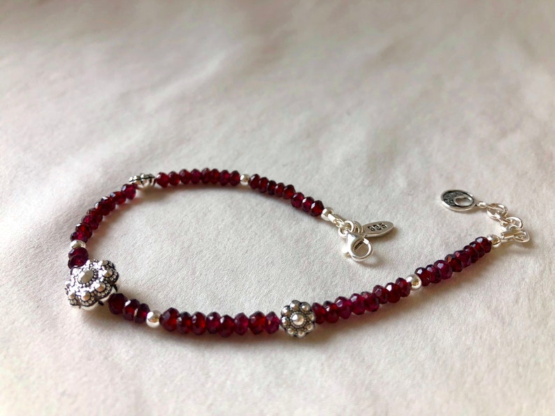 May include: A silver bracelet with a red gemstone bead chain and silver flower charms.