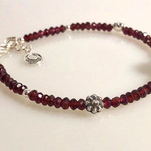 May include: A silver bracelet with red garnet beads and two silver flower charms.