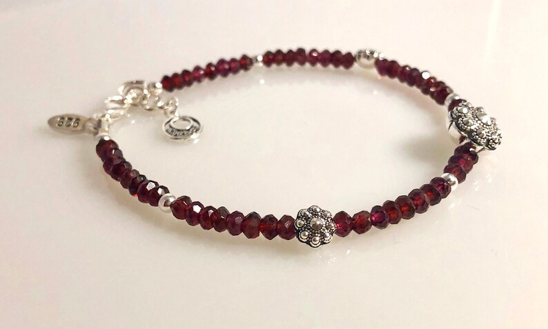 May include: A silver bracelet with red garnet beads and two silver flower charms.