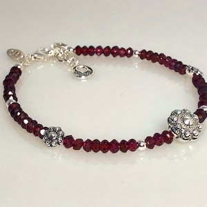 May include: A silver bracelet with red gemstone beads and two silver flower charms.