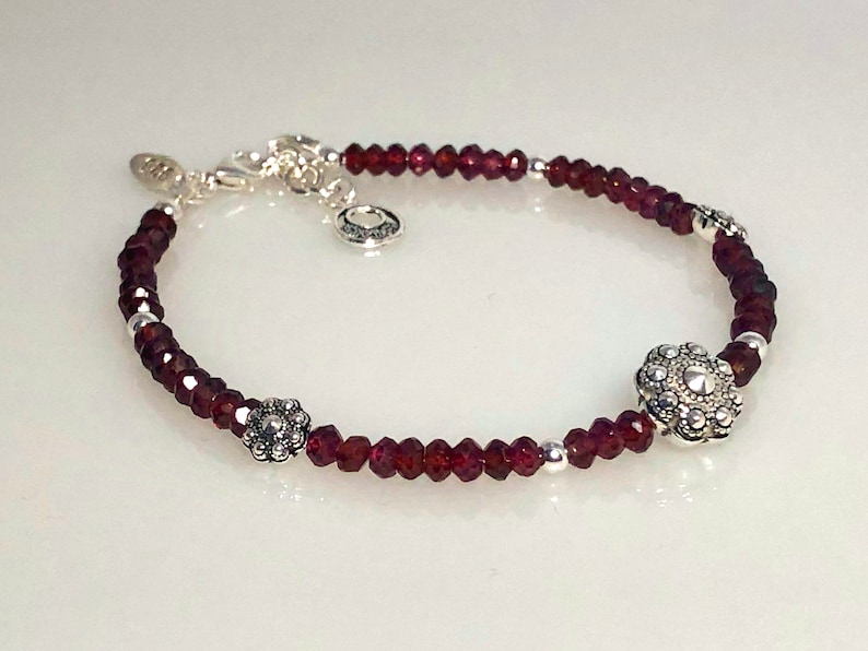 May include: A silver bracelet with red gemstone beads and two silver flower charms.