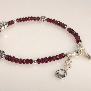May include: A silver bracelet with a clasp and three silver flower charms. The bracelet is made with small, dark red garnet beads.