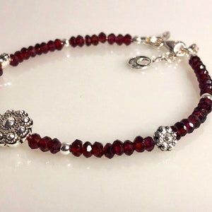 May include: A silver bracelet with red garnet beads and two silver flower-shaped charms.