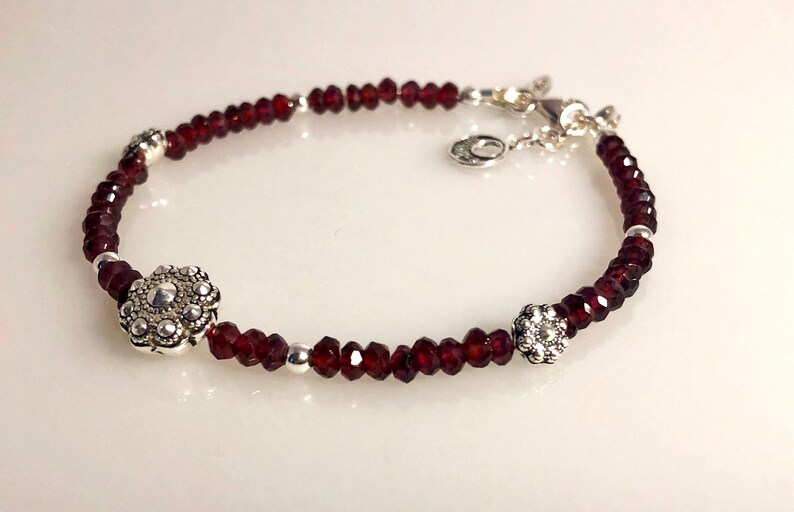 May include: A silver bracelet with red garnet beads and two silver flower-shaped charms.