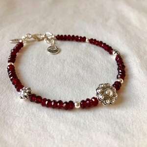 May include: A red beaded bracelet with silver accents. The bracelet has two silver flower-shaped charms.