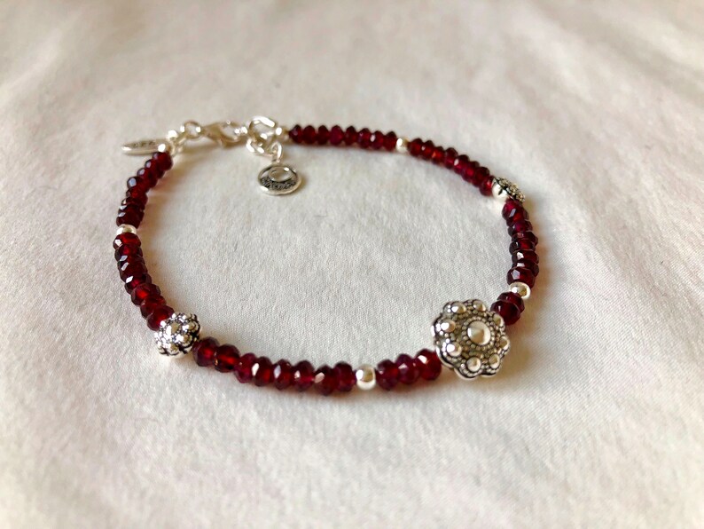 May include: A red beaded bracelet with silver accents. The bracelet has two silver flower-shaped charms.