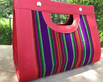 May include: A red leather handbag with a woven fabric panel featuring colourful stripes in shades of green, purple, pink, and orange. The bag has a top handle and a flap closure.