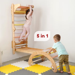 May include: A wooden play structure with a climbing wall, a slide, and a ladder. The structure is designed for children to climb, slide, and play. The structure is made of natural wood and has a light brown finish. The structure is labelled "5 in 1".