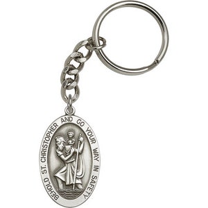 May include: Silver key chain with a round oval charm featuring a depiction of Saint Christopher carrying a child. The charm has the text "Behold St. Christopher and go your way in safety".