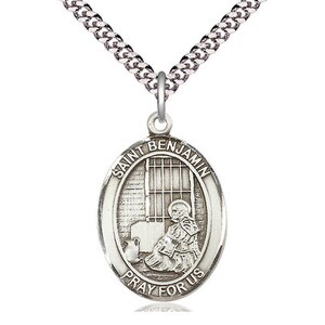 May include: Silver Saint Benjamin pendant necklace. The oval pendant features an image of Saint Benjamin in front of a barred window, with the words "Saint Benjamin" and "Pray for Us" around the edge. The pendant hangs from a silver chain.