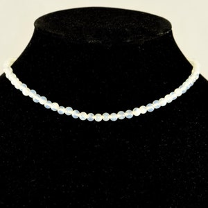 May include: A white beaded necklace displayed on a black velvet stand.