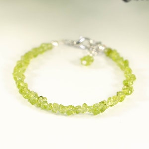 May include: A green peridot gemstone bracelet with a silver clasp. The bracelet is made of small, irregularly shaped peridot stones.