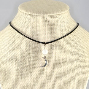 May include: A black choker necklace with a silver crescent moon charm and a white bead.