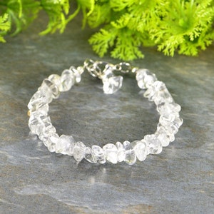 Peut inclure: Un bracelet en cristal de roche clair avec un fermoir argenté. Le bracelet est sur un fond gris.