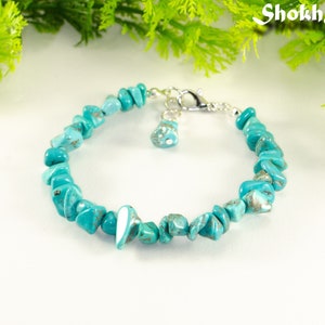 Peut inclure: Bracelet en pierres turquoise avec un fermoir argenté et un petit charme turquoise. Le bracelet est composé de pierres turquoise de forme irrégulière.