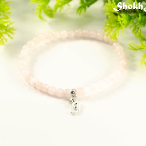 Peut inclure: Un bracelet en quartz rose rose avec un charme argenté. Le bracelet est composé de petites perles rondes et est enfilé sur un cordon élastique transparent. Le charme est un petit pendentif argenté en forme de croissant de lune.