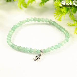May include: A light green beaded bracelet with a silver charm in the shape of the letter 'S'.