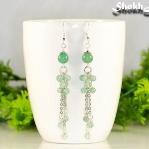 May include: A pair of silver dangle earrings with green gemstone beads. The earrings feature multiple strands of chain with small green beads hanging from the larger bead.