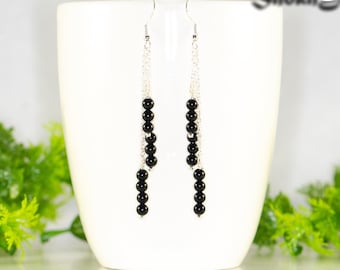 May include: Silver chain earrings with black beads hanging from a white ceramic cup. Shokh Jewelry is written in the top right corner of the image.