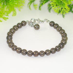 May include: A bracelet featuring dark, metallic-colored beads. The beads are strung together with a silver-colored chain and clasp. The text "Shokh Jewelry" is visible in the upper right corner. The bracelet is displayed against a white background.