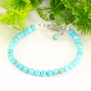 May include: A turquoise beaded bracelet with a silver clasp. The bracelet is made of round, light blue beads. The background features green foliage and the text "Shokh Jewelry".