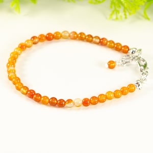 Peut inclure: Un bracelet délicat en pierre de cornaline orange avec un fermoir argenté. Le bracelet est composé de petites perles rondes et présente un design simple et élégant.