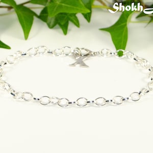 May include: A silver chain bracelet with a silver letter X charm.
