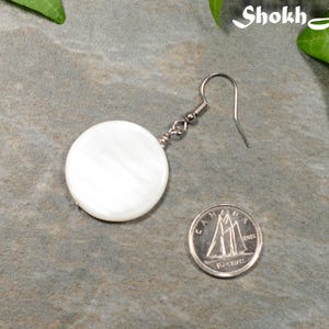 May include: A white round shell earring with a silver hook. The earring is about the size of a Canadian dime.