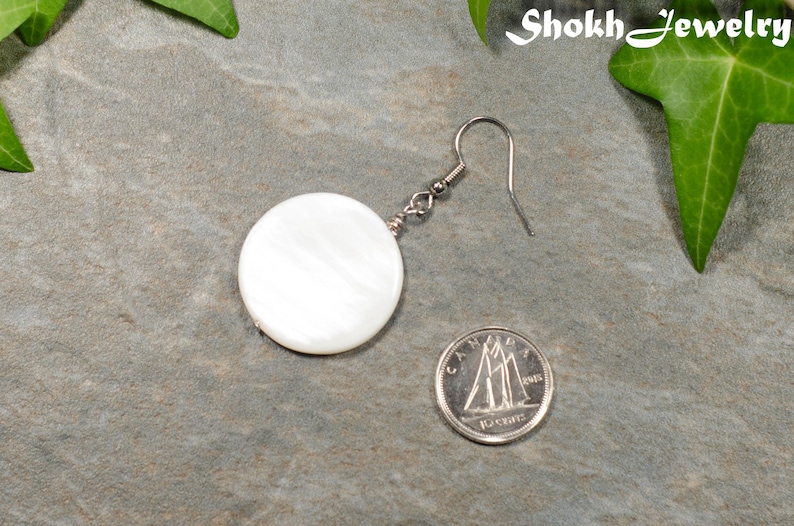 May include: A white round shell earring with a silver hook. The earring is about the size of a Canadian dime.