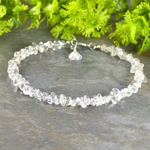 May include: A delicate clear quartz chip necklace with a silver clasp. The necklace is made of small, irregular pieces of quartz that are strung together on a silver chain.