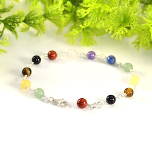 May include: A silver chain bracelet with seven colorful gemstone beads. The beads are red, orange, yellow, green, blue, indigo, and violet.
