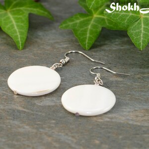 May include: A pair of white shell earrings with silver hooks. The earrings are round and have a smooth, polished finish.