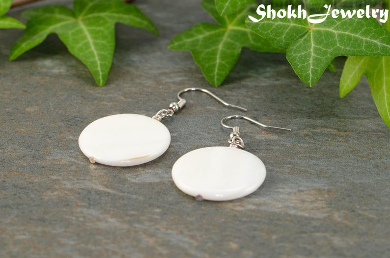 May include: A pair of white shell earrings with silver hooks. The earrings are round and have a smooth, polished finish.