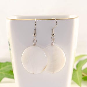 May include: A pair of white shell earrings with silver hooks. The earrings are round and have a smooth, polished finish.