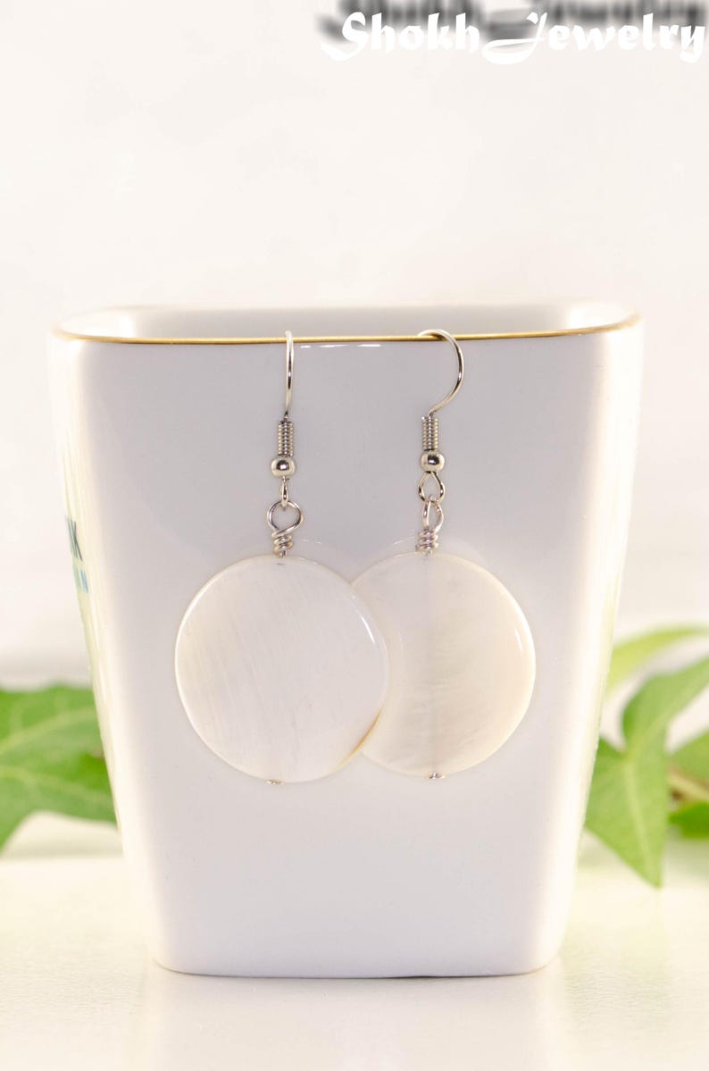 May include: A pair of white shell earrings with silver hooks. The earrings are round and have a smooth, polished finish.